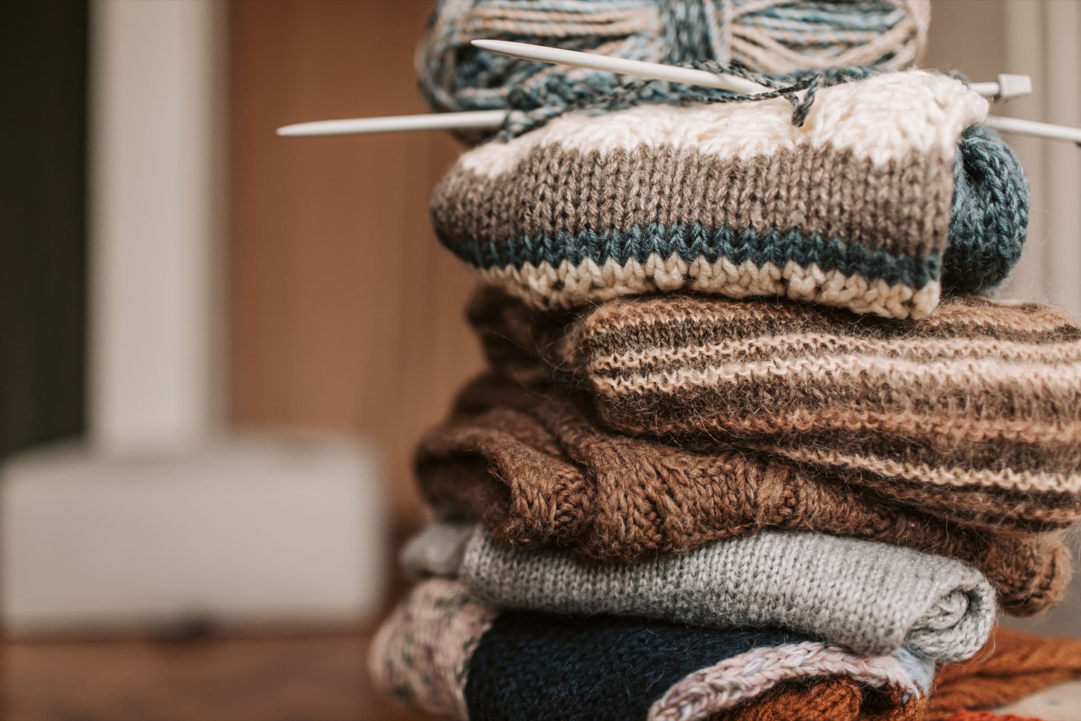 Stapel handgestrickter Kleidungsstücke mit Wolle und Stricknadeln